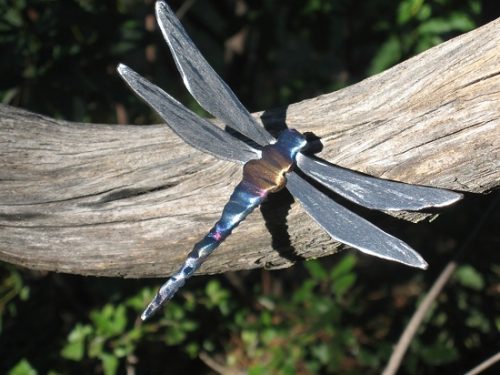 Handcrafted metal dragonfly by John Running displayed on a branch outside.