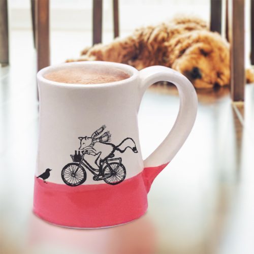 Red and white ceramic mug featuring a fox delivering beers on his bicycle.