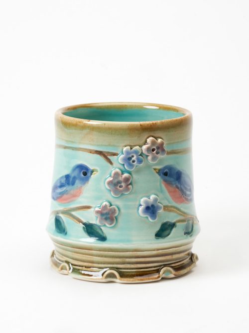 Ceramic bluebird mug by Bluegill Pottery with hand-carved branches and flowers.