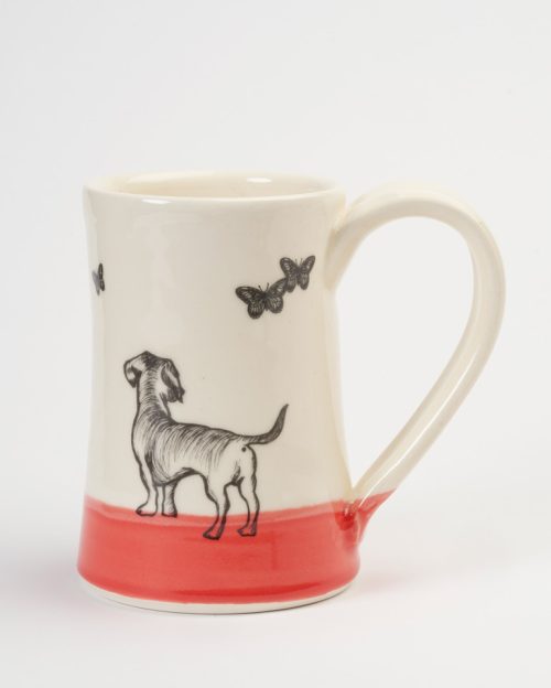 A ceramic coffee mug handmade by Darn Pottery featuring a dog chasing butterflies.