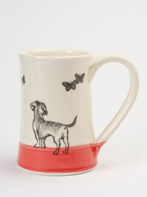 A ceramic coffee mug handmade by Darn Pottery featuring a dog chasing butterflies.