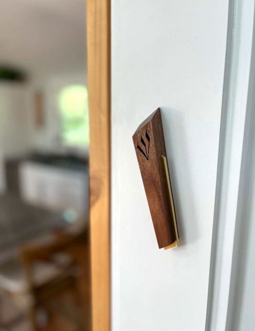 A wooden and brass mezuzah handcrafted by Windthrow hanging in a doorway.