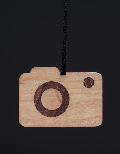 A simple wooden camera ornament on a black background.