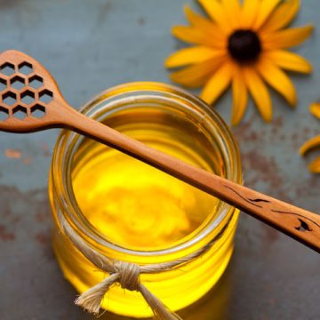 A handmade wooden honey stick sitting on top of a honey jar.