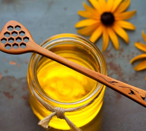 A handmade wooden honey stick sitting on top of a honey jar.