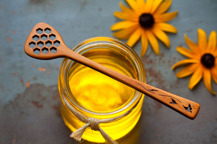 A handmade wooden honey stick sitting on top of a honey jar.