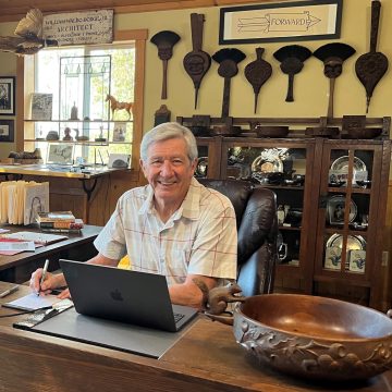 Asheville historian Bruce Johnson sitting at the laptop in his home office surrounded by examples of Biltmore Industries woodcarvings.