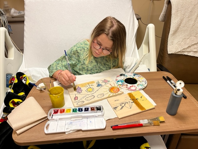 Arts For Life client working on a painting in a hospital bed.