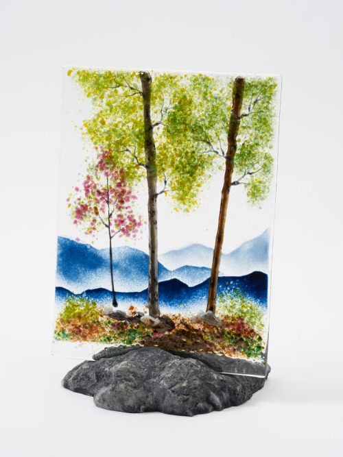 A fused glass spring mountain scene with a rock base holder by Amanda Taylor.