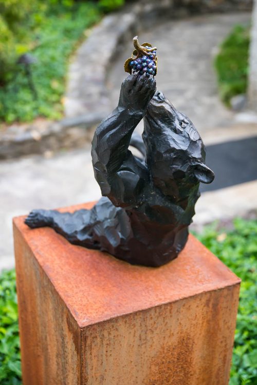 Outdoor sculpture by Roger Martin featuring a bronze bear eating grapes.