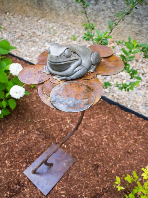 An outdoor sculpture featuring a bronze frog on a steel lily pad titled Fly Fishing by Todd Frahm.