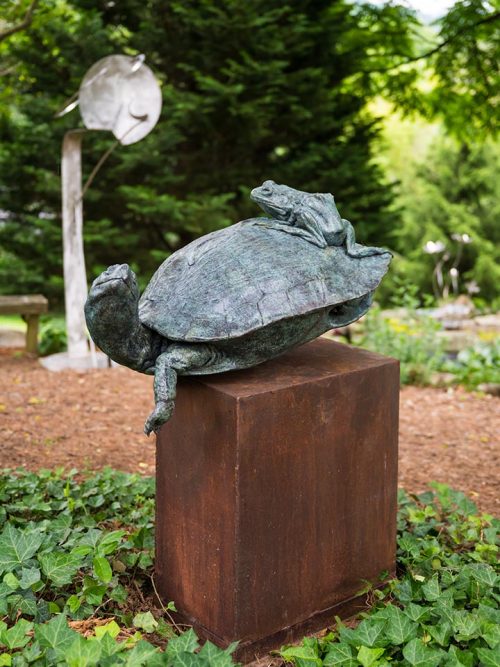 An outdoor sculpture titled The Interloper featuring a large turtle with a frog riding on his back.