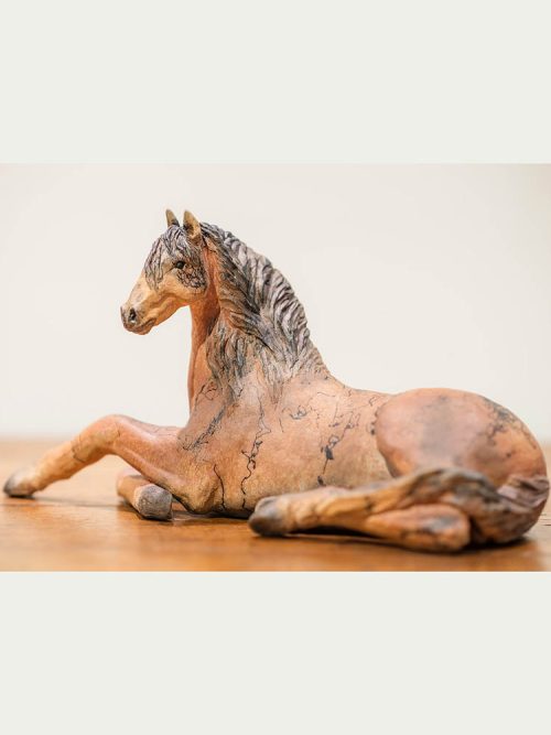 A handcrafted reclining horse sculpture by Tina Curry.